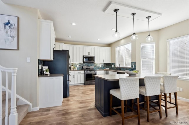 kitchen featuring decorative light fixtures, white cabinets, light wood-type flooring, and appliances with stainless steel finishes