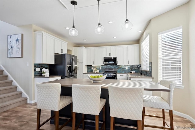 kitchen with decorative light fixtures, stainless steel appliances, a kitchen island, white cabinetry, and sink