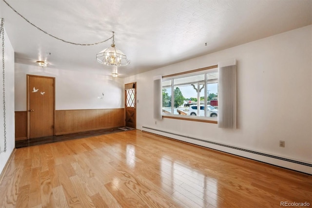 209 S 13th Ave, Brighton, CO 80601 - empty room featuring baseboard heating, wood finished floors, a wainscoted wall, a chandelier, and wood walls