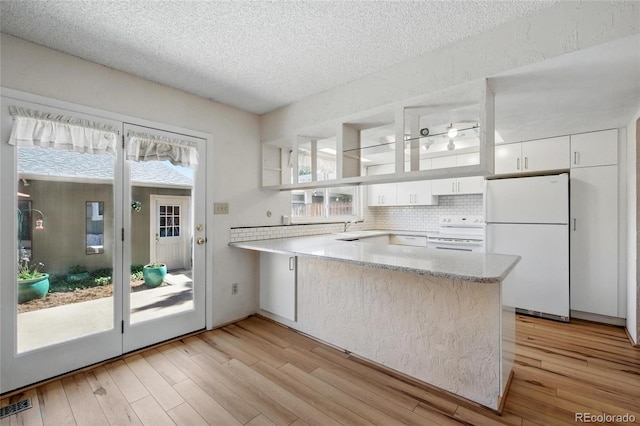 kitchen featuring white appliances, a peninsula, white cabinets, tasteful backsplash, and plenty of natural light