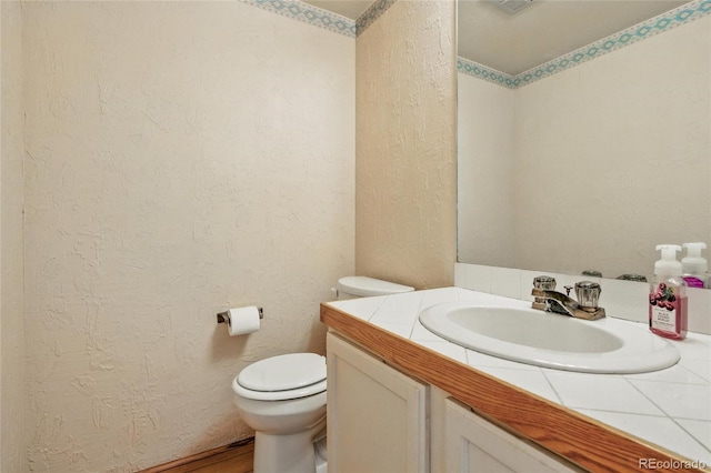 half bath with a textured wall, toilet, and vanity