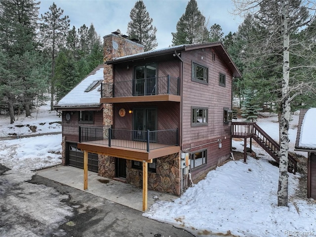 snow covered back of property featuring a balcony and a garage