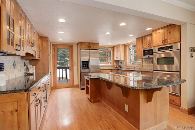 kitchen with a center island, dark stone counters, a kitchen breakfast bar, decorative backsplash, and stainless steel appliances