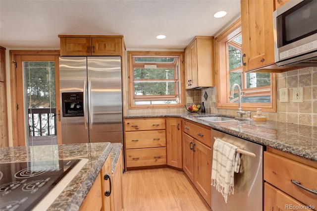 kitchen featuring light hardwood / wood-style floors, sink, stainless steel appliances, and dark stone counters