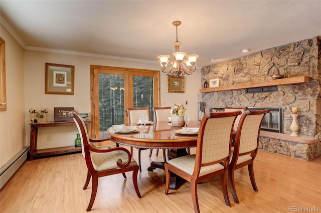 dining space with a baseboard heating unit, crown molding, an inviting chandelier, light hardwood / wood-style flooring, and a stone fireplace