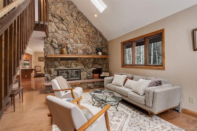 living room with a fireplace, high vaulted ceiling, a skylight, and light hardwood / wood-style flooring