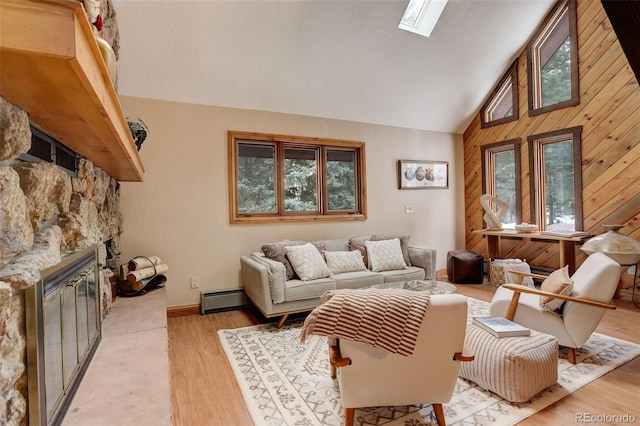 living room with a skylight, baseboard heating, wooden walls, light hardwood / wood-style flooring, and a stone fireplace