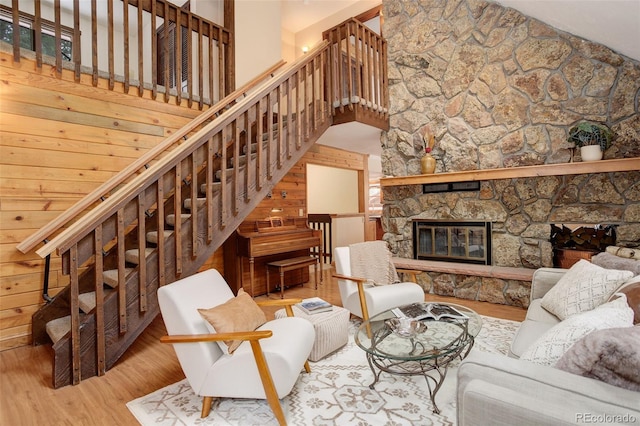 living room featuring a stone fireplace, wooden walls, light hardwood / wood-style flooring, and a high ceiling