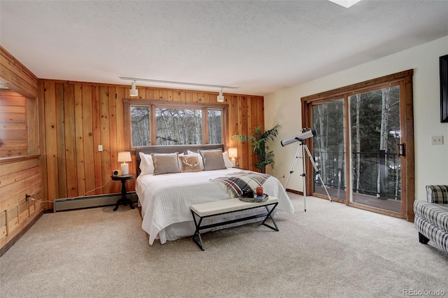 carpeted bedroom with baseboard heating, access to exterior, wooden walls, and track lighting