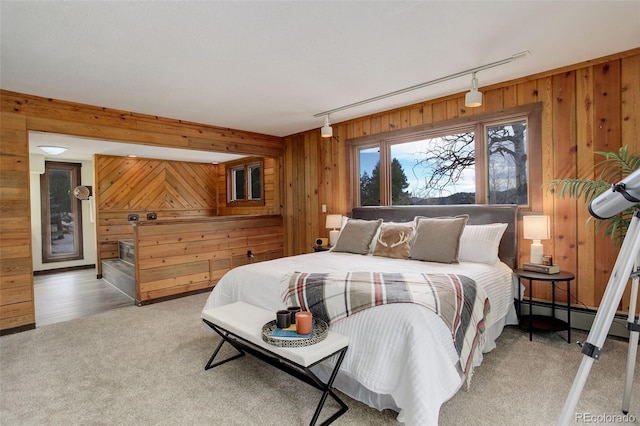 carpeted bedroom featuring rail lighting, a baseboard radiator, and wooden walls