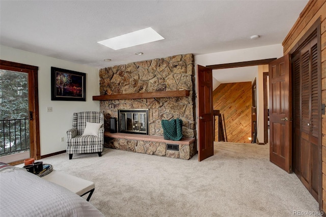 living room with a stone fireplace, wooden walls, carpet floors, and a skylight