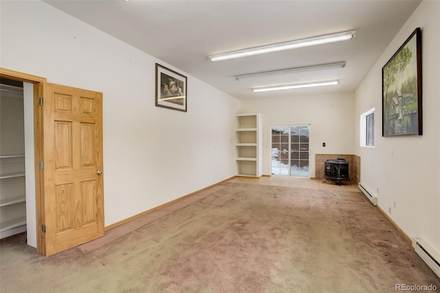 unfurnished living room with carpet flooring, a wood stove, and a baseboard heating unit