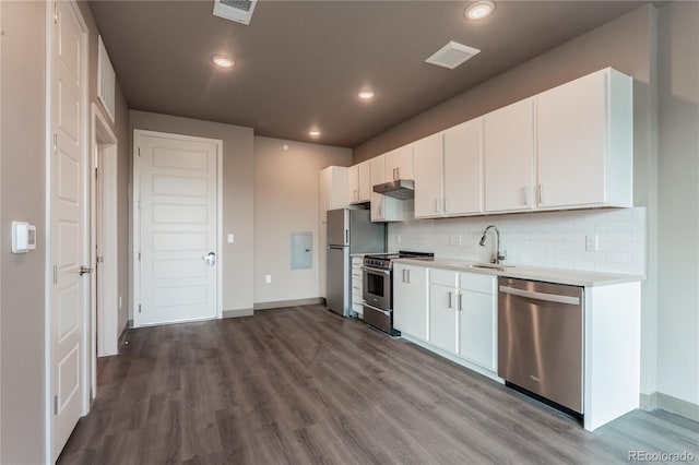 kitchen with appliances with stainless steel finishes, sink, white cabinetry, hardwood / wood-style flooring, and decorative backsplash