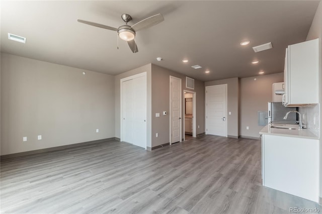 kitchen with sink, backsplash, ceiling fan, white cabinets, and light hardwood / wood-style flooring