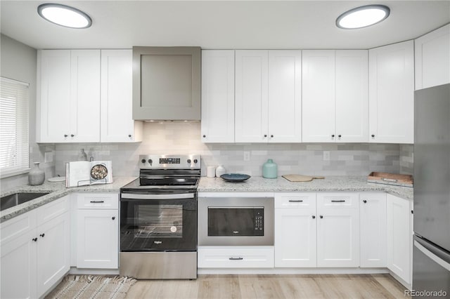 kitchen featuring light hardwood / wood-style flooring, appliances with stainless steel finishes, tasteful backsplash, light stone counters, and white cabinets