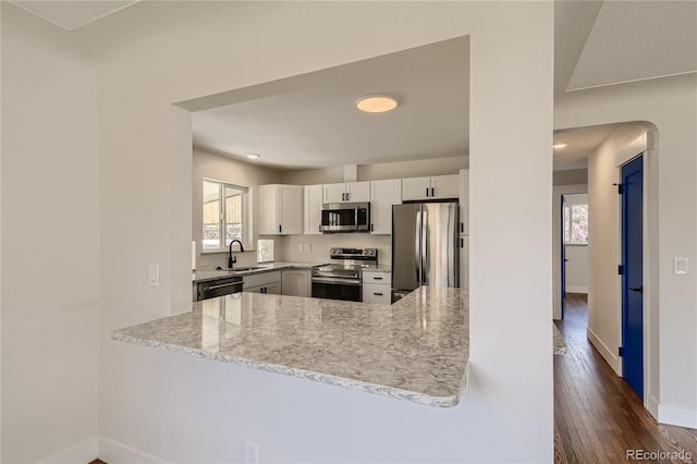 kitchen with appliances with stainless steel finishes, white cabinetry, sink, kitchen peninsula, and light stone countertops