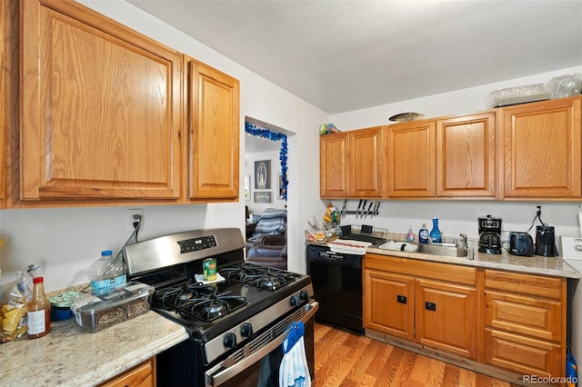 kitchen featuring stainless steel gas range oven, black dishwasher, light stone countertops, light hardwood / wood-style flooring, and sink