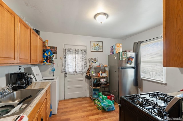 kitchen featuring gas stove, light wood-type flooring, stainless steel refrigerator, washer / clothes dryer, and sink