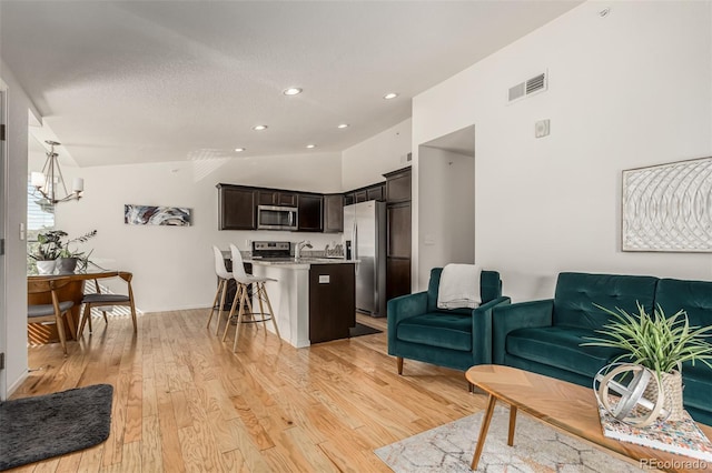 living room featuring lofted ceiling, an inviting chandelier, light hardwood / wood-style floors, and a textured ceiling