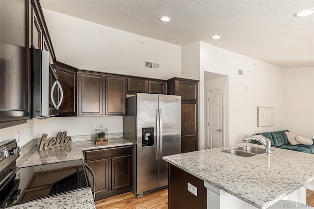 kitchen featuring a center island with sink, light hardwood / wood-style floors, light stone countertops, and stainless steel appliances