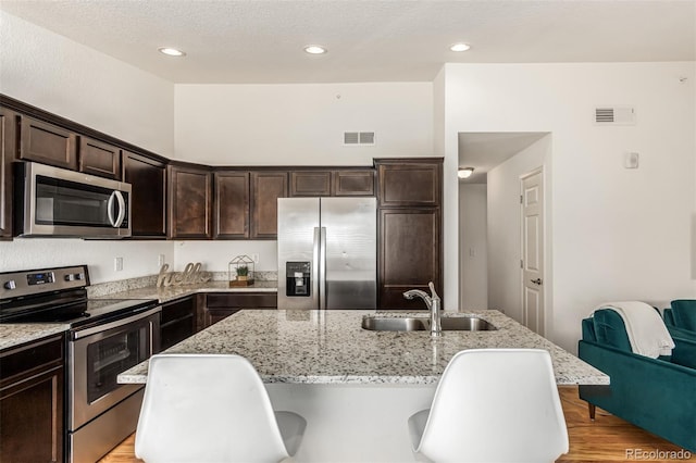 kitchen with light stone countertops, appliances with stainless steel finishes, light wood-type flooring, and sink