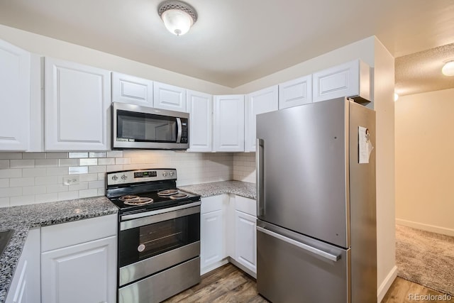 kitchen featuring appliances with stainless steel finishes, tasteful backsplash, white cabinetry, light stone counters, and light wood-type flooring