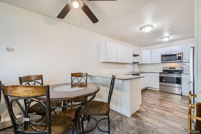 kitchen featuring white cabinetry, light hardwood / wood-style flooring, kitchen peninsula, sink, and appliances with stainless steel finishes