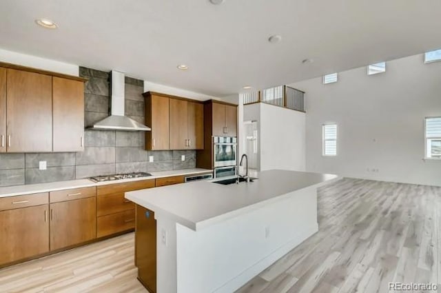 kitchen with stainless steel gas stovetop, a center island with sink, light hardwood / wood-style floors, and wall chimney range hood