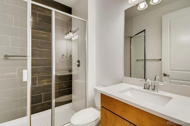 bathroom with a shower with shower door, vanity, and toilet