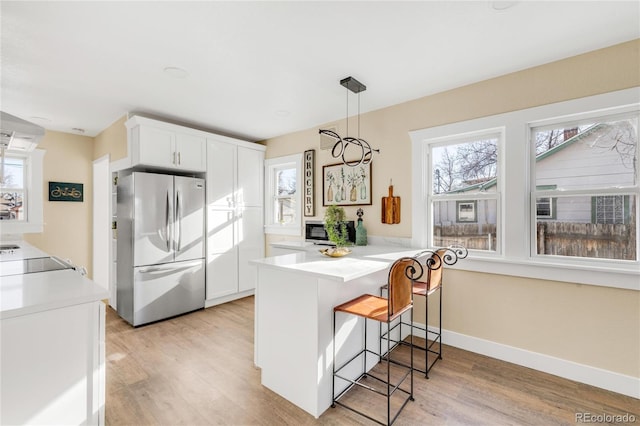 kitchen featuring white cabinets, stainless steel fridge, light hardwood / wood-style floors, kitchen peninsula, and a breakfast bar area