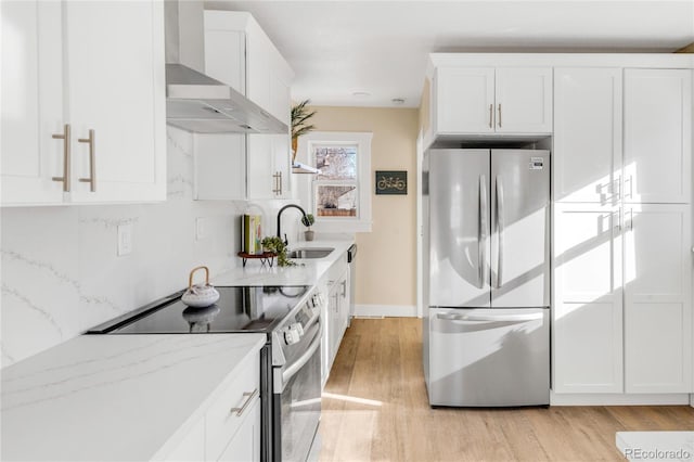 kitchen with sink, wall chimney range hood, light stone counters, white cabinets, and appliances with stainless steel finishes