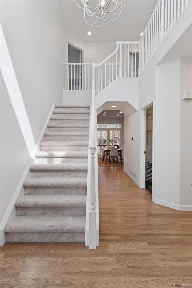 stairway with baseboards, an inviting chandelier, wood finished floors, and recessed lighting