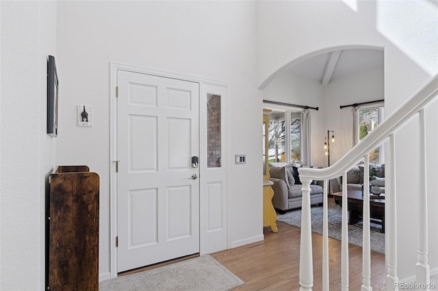 foyer entrance with baseboards, arched walkways, vaulted ceiling with beams, and light wood-type flooring
