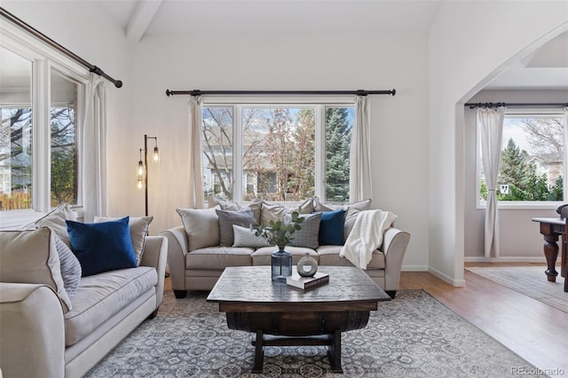 living room with arched walkways, baseboards, beam ceiling, and wood finished floors