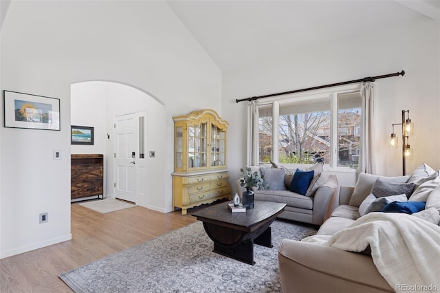 living area with high vaulted ceiling, arched walkways, wood finished floors, and baseboards