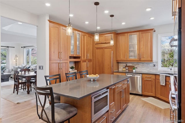 kitchen with dark countertops, decorative backsplash, a breakfast bar area, stainless steel appliances, and light wood finished floors