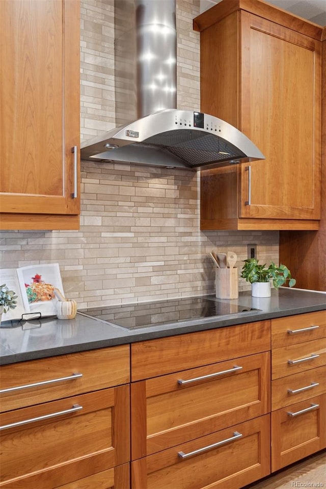 kitchen featuring wall chimney exhaust hood, brown cabinetry, black electric stovetop, and tasteful backsplash