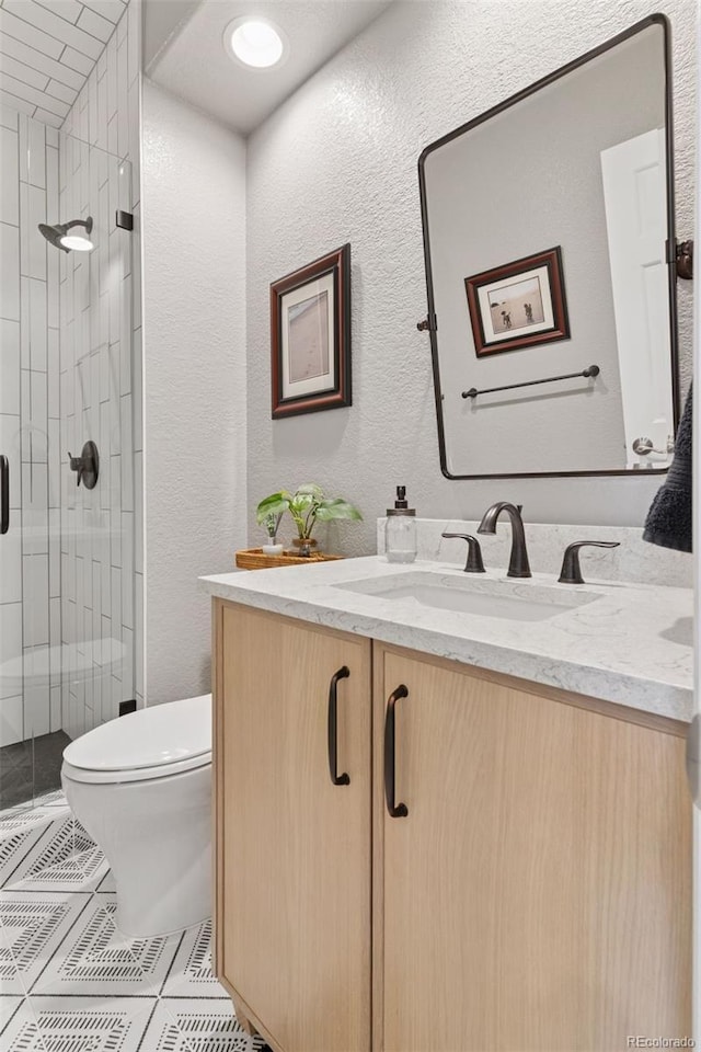 full bath with a shower stall, a textured wall, toilet, and vanity
