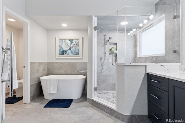 full bathroom with a shower stall, toilet, vanity, tile walls, and a soaking tub