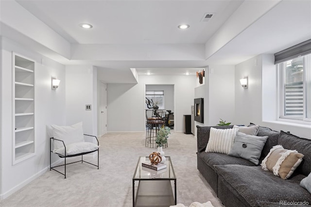living area with light carpet, a warm lit fireplace, visible vents, and a healthy amount of sunlight