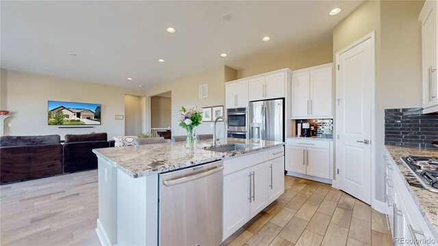 kitchen featuring stainless steel appliances, white cabinetry, a center island with sink, and sink