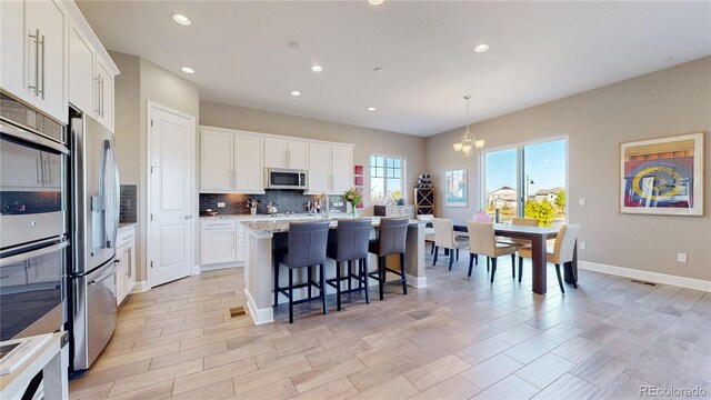 kitchen with white cabinetry, an inviting chandelier, a center island with sink, appliances with stainless steel finishes, and decorative light fixtures