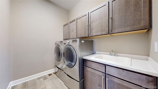 laundry area featuring cabinets, light hardwood / wood-style floors, sink, and washer and dryer