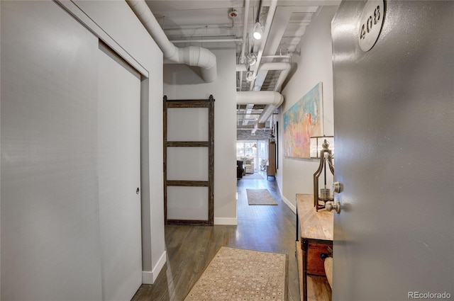 hallway with wood finished floors, a towering ceiling, baseboards, and a barn door