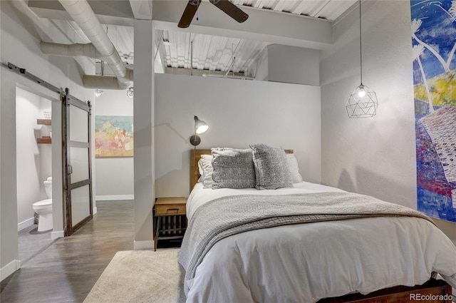 bedroom featuring ensuite bath, a barn door, baseboards, and wood finished floors