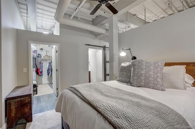 bedroom with a barn door, ceiling fan, wood finished floors, a walk in closet, and a closet