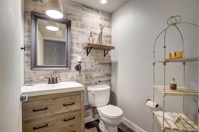 half bathroom featuring toilet, baseboards, and vanity