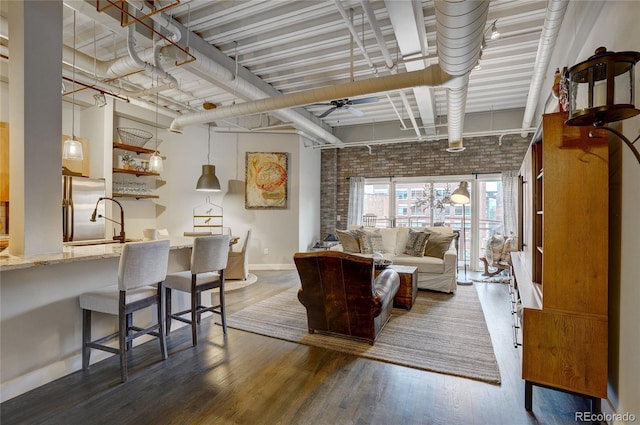 interior space with brick wall, wood finished floors, a ceiling fan, and baseboards