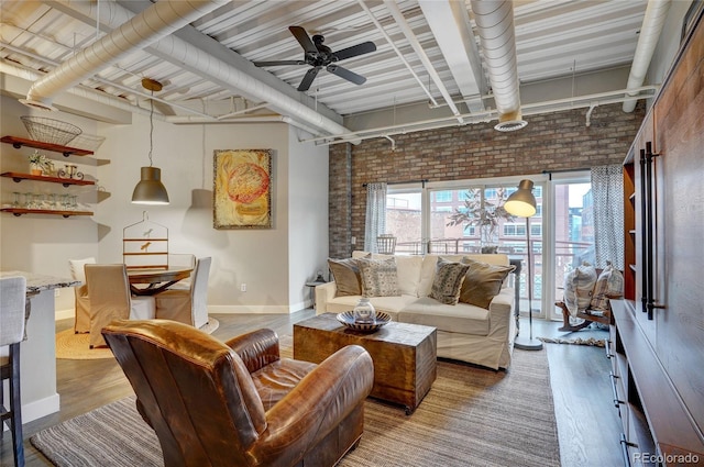 living room featuring a ceiling fan, baseboards, brick wall, and wood finished floors