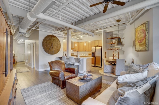 living area featuring a ceiling fan, a towering ceiling, light wood-style flooring, and baseboards